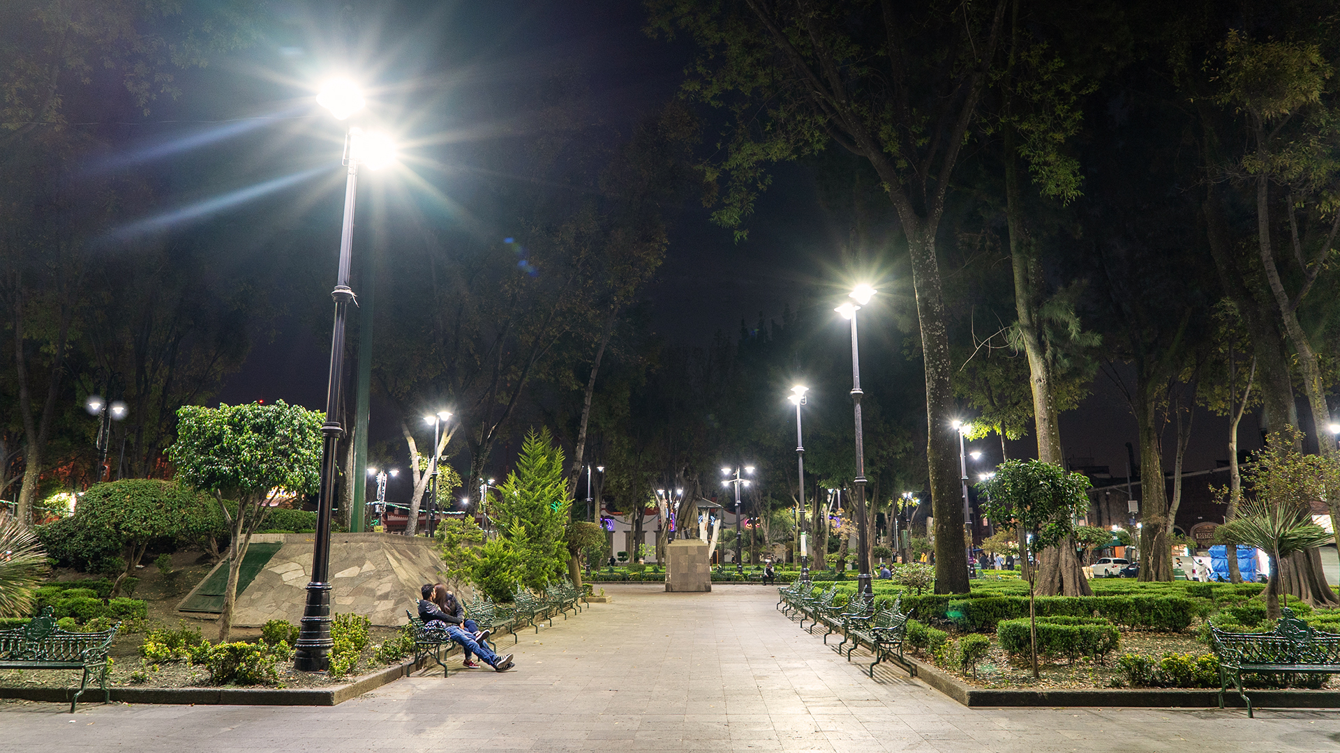 Personas sentadas en banca del parque en zona segura con iluminación de Espacios Recreativos Coyoacán