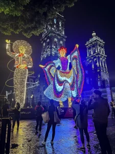 Figuras de luz Monumentales de charro y bailarina en el zócalo de Puebla durante las fiestas patrias. De fondo las torres de Catedral con iluminación dinámica generando photomoments